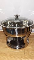 Chafing dish assembled on stand, showing polished stainless steel sides and glass lid with handle.