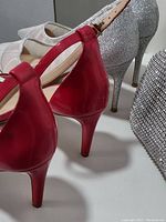 Back view of the pink and silver women's heeled shoes showing heel height and glossy finish, next to the silver rhinestone purse.