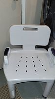 White plastic shower chair with backrest and armrests.