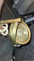 Close-up of the compass with visible cardinal directions under glass cover and attached rope handle, showing brass frame details.