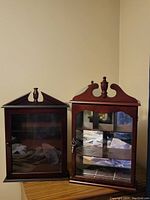 Front view of two wooden display cabinets with glass doors and decorative finials on top.