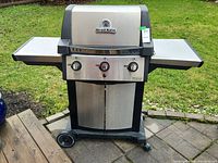 Full view of the Broil King propane BBQ grill showing stainless steel body, two side shelves, and front control panel with three knobs.