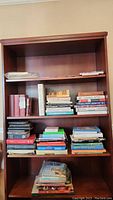 Four wooden shelves with assorted novels, magazines, and a new Bible in package on top shelf