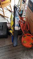 Photo showing black tool kit case, umbrella or carrying bag, jumper cables, orange extension cord, and part of rocking chair