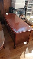 Side angle of cedar lined wooden chest showing two ornate handles and reddish brown finish.