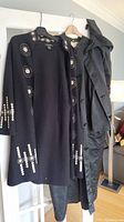 Black wool sweater with white circular patterns hanging beside a black rain jacket.