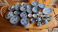 Full view of the dinnerware set arranged on wooden table, showing plates, bowls, cups, teapots, creamer, and sugar bowl with blue floral patterns.