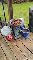 Image showing black decorative pedestal planter with garden stones, blue ceramic pots, cement shoe planter, round cement stone and ladybug ornament.