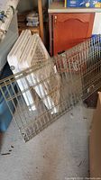 White expanding baby gates leaning against a wall next to wooden furniture.