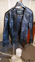 Front view of the black leather Danier jacket showing fringe tassels at hem and cuffs, hanging on a hanger.