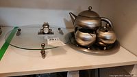 Full view of metal coffee set and glass serving platter with frog clock on top