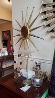 Starburst mirror on stand with various vases and metallic glass decorations on a dark wood table