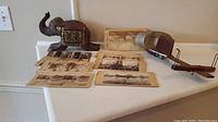 Full view of the stereoscope with assorted stereoscopic cards and wooden elephant box on a white surface.