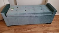 Side view of light blue padded bench showing armrest, tufted top, and fabric texture.