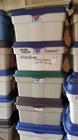 Stacked plastic storage bins showing labels and different colored lids