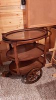 Side view of wooden tea trolley showing large spoked wooden wheel and three shelves.