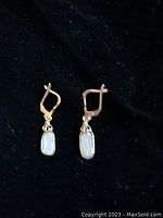 Photo of both earrings laying flat on black background showing rectangular pearls and lever-back clasps, focusing on detail of pearls and gold setting.