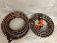 Two coiled Black & Decker garden hoses laid side by side, one with an orange and black handheld spray nozzle attached.