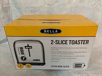 Box front showing Bella brand 2-slice toaster with key features: 6 setting shade control dial, red illuminated control buttons, high-lift lever, extra-wide slots, 900 watts power, BPA free, 2-year warranty.