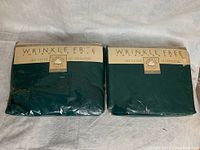 Two dark green twin deep fitted sheets sealed in original plastic packaging labeled Wrinkle Free by Cotton Inc.