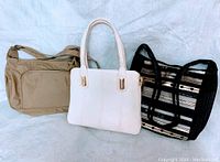 Three handbags: beige shoulder bag, white handbag, and black-beige striped tote, arranged side by side.