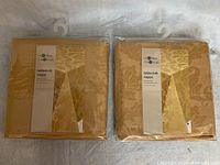 Two yellow tone on tone damask tablecloths in original packaging with hangers visible, showing brand Life@Home.