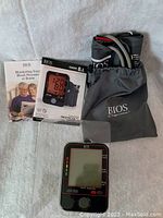 Top-down view showing the digital blood pressure monitor, instruction manual, carrying case, and cuff laid out on a gray background.