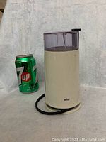 Braun coffee/spice grinder shown next to a 7up can for size comparison, featuring white body and black power cord.