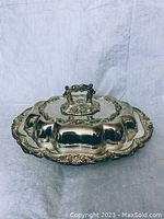 Closed view of two-piece covered silver dish showing decorative lid with handle and scalloped edges