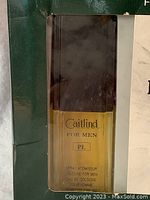 Close-up photo of the cologne bottle - rectangular bottle with black cap, yellow liquid inside, labeled Caitlind For Men PL Spray Atomiseur Cologne.