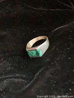 Silver ring with rectangular turquoise stone inset, shown on a dark background.