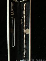 Tennis bracelet displayed in a box with a coin to show scale, showing the cubic zirconia stones and gold color metal
