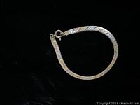 Photo of tri-coloured herringbone pattern flat link bracelet against black background showing spring ring clasp and design details.