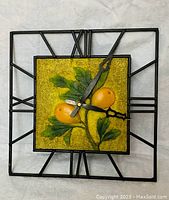 Front view of square clock with wrought iron Roman numeral frame and tile center featuring yellow-orange fruits and green leaves.