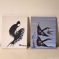 Photo showing a pair of Randy Knott original paintings 8x10 inches each, one with a single black stylized bird on white and the other with three flying birds on blue-gray background