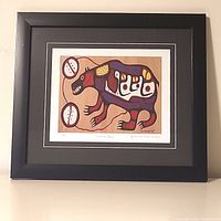 Framed Norval Morrisseau 'Sacred Bear' limited edition art print hung on wall, showing full artwork with black frame and matting.