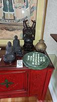 Arrangement of all items on red table showing Buddha statues, brass bell and marble Chinese checker board with marbles.