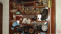 Front-on view of multi-tiered wooden display shelf holding brass, bronze and stone figurines