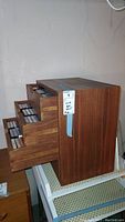 Wooden storage chest with three drawers open, containing cassette tapes.