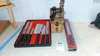 Overall lot arrangement on countertop: Sabatier knife set in red foam tray at left, wooden block with steak knives and steel in center, Sabatier slicer in sleeve at right