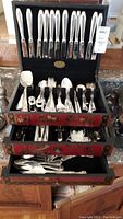 Front view of open storage box showing knives in top rack and various forks, spoons arranged below, and storage drawers partially open.