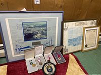Photo showing four military medals in cases and a round cloth patch, alongside three framed prints behind them