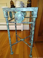 Front view of the metal stand showing the weathered green patina finish, decorative circular accents, and beveled glass top.