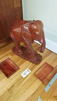Wood carved elephant statue and two polished wooden bowls placed on hardwood floor next to door and baseboard.