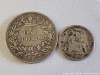 Two European silver coins from the 1830s, one a clearly visible One Shilling coin dated 1838 with crown and leaf wreath, the other smaller and heavily worn with visible date 1838.