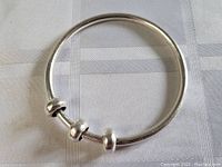 Full view of the polished sterling silver bangle bracelet with three rounded sliding beads shown on light fabric background.