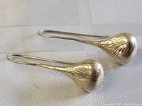 Pair of sterling silver teardrop-shaped earrings displayed on white fabric. Carved and etched floral designs visible on convex surfaces.