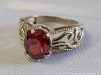 Close up front view of oval ruby in sterling silver ring with ornate filigree sides.