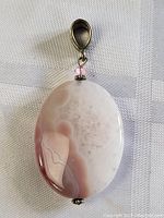 Front view of oval stone pendant showing polished surface, color variations and sterling silver fittings.