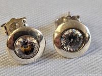 Close-up photo of sterling silver stud earrings showing polished silver surfaces and clear stones.